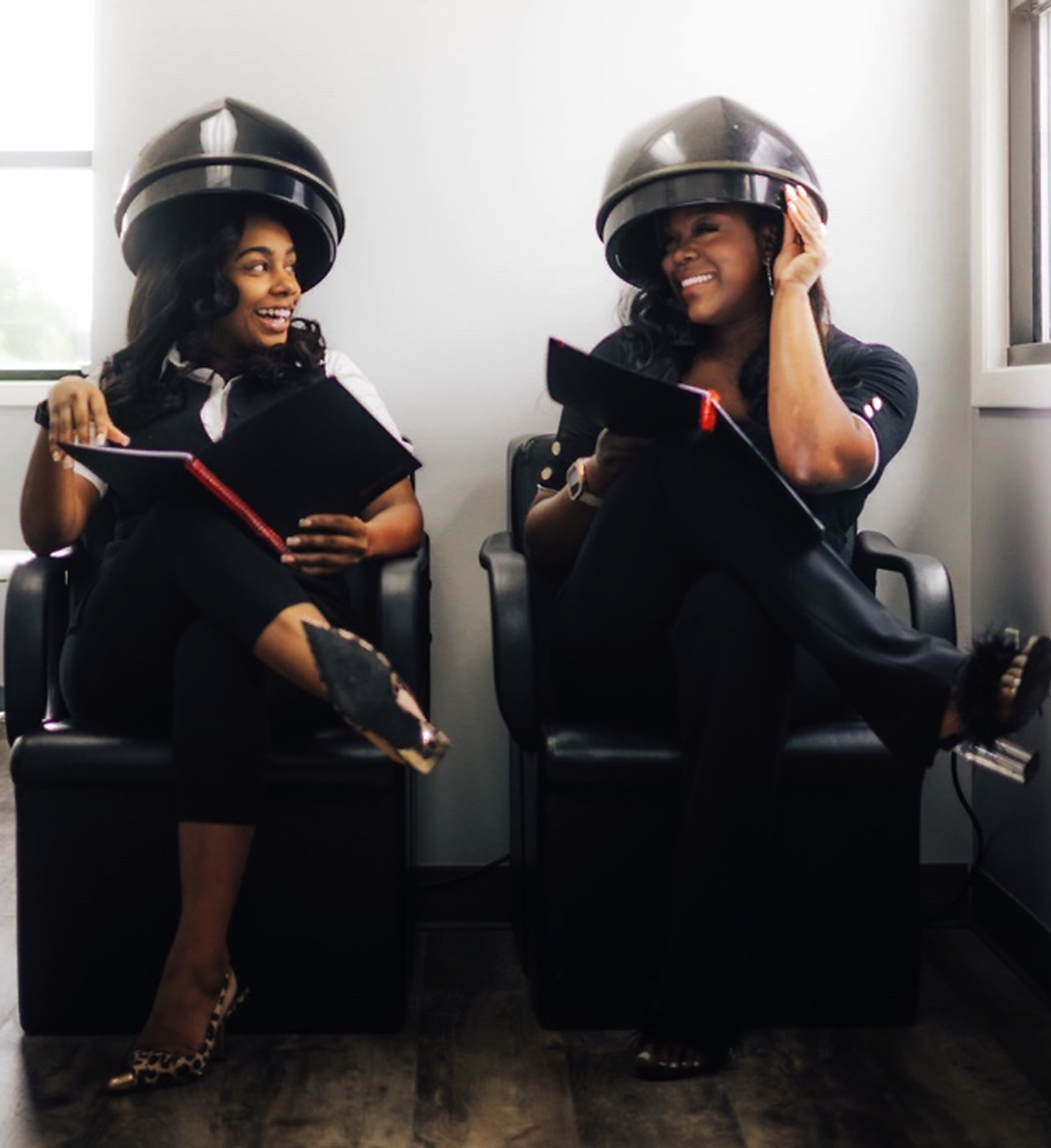 Two guests laughing together under salon hooded dryers